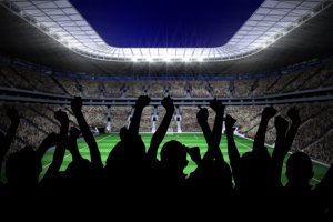 Silhouettes of football supporters against large football stadium with lights